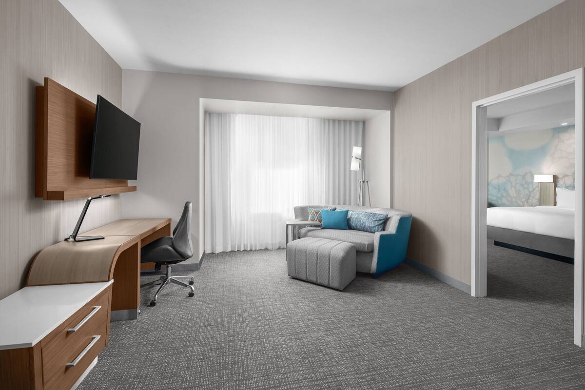 A hotel room with a desk, chair, bed, and a television mounted on the wall.