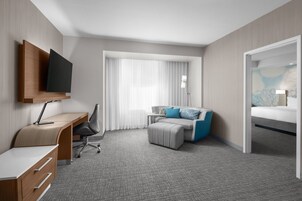 Una habitación de hotel con escritorio, silla, cama y televisor montado en la pared.
