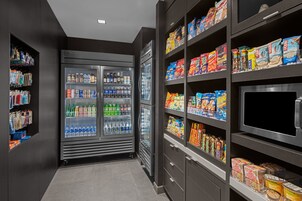 A modern hotel lobby with a refrigerated beverage display, snack shelves, and a flat-screen TV.