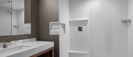 A modern bathroom with a large mirror, a white sink, a wooden vanity, a shower with a rain showerhead, and a towel rack.