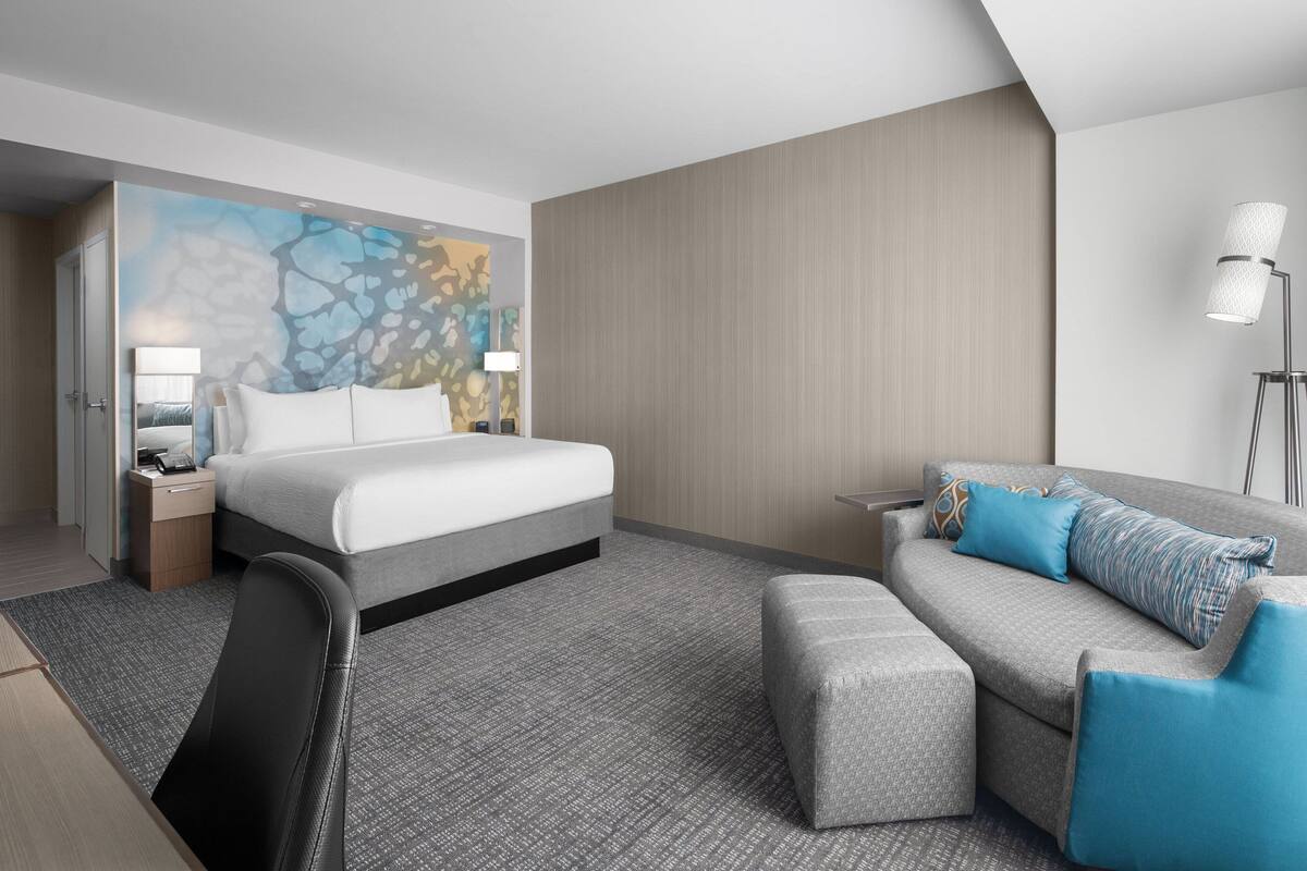 A modern hotel room with a large bed, a sofa, and a desk.