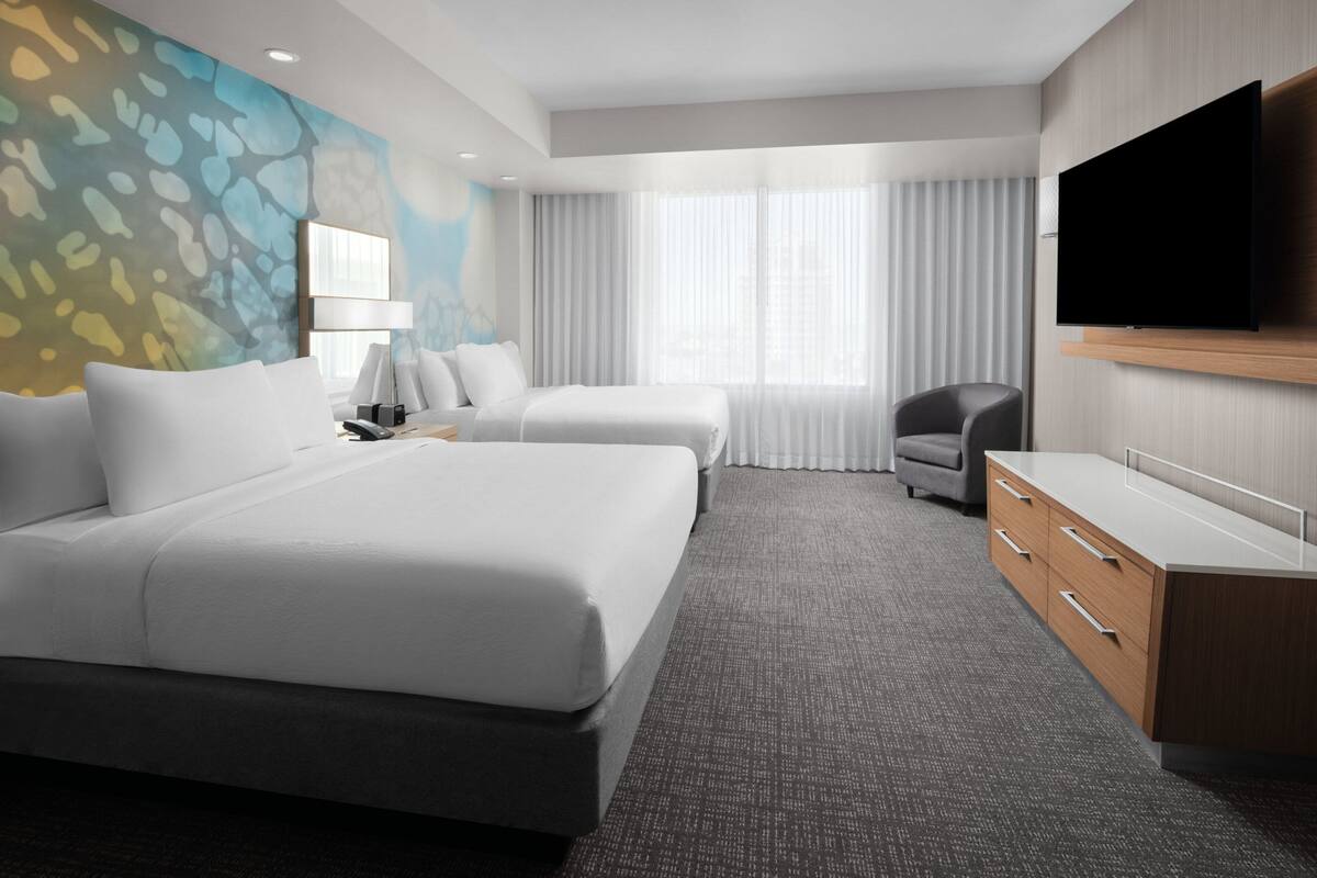 A modern hotel room with two beds, a flat-screen TV, a desk, and a chair.
