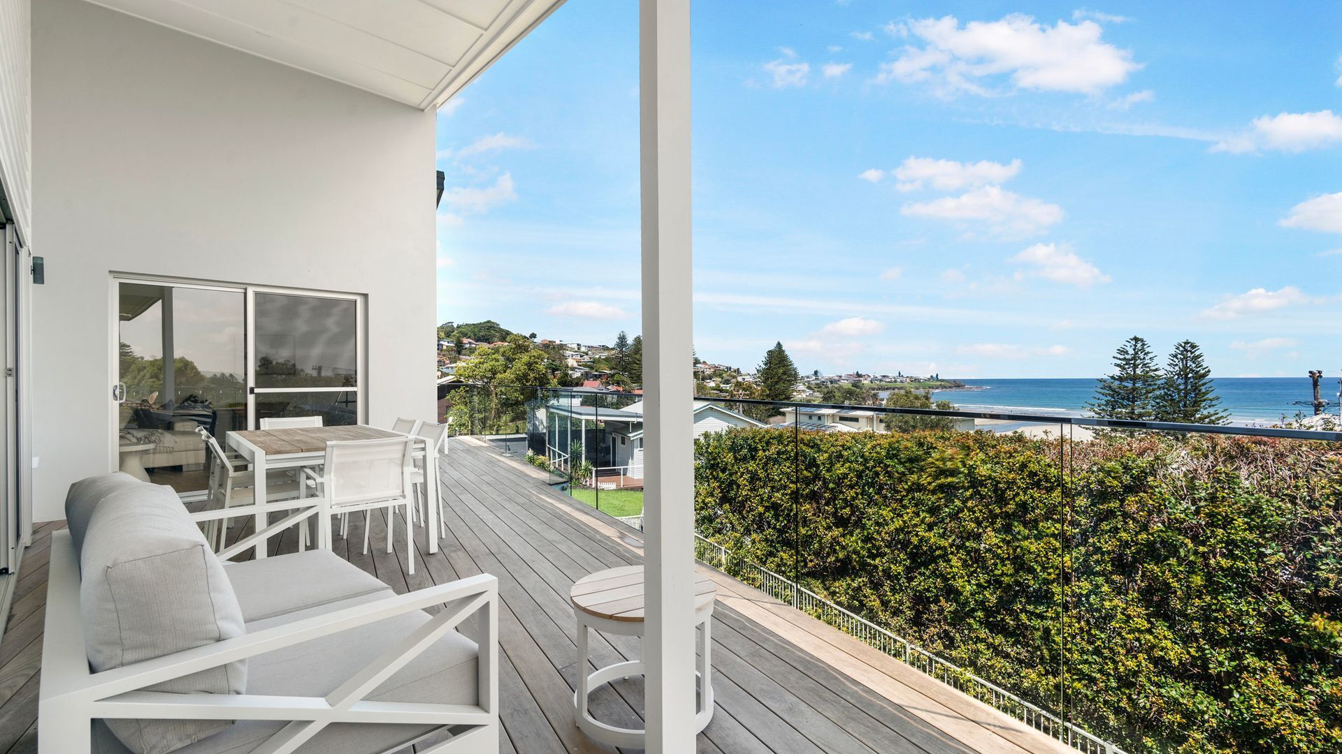 Un balcon avec vue sur la mer, un espace extérieur aménagé avec des sièges blancs et une haie.