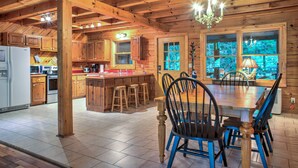 A wooden cabin interior with a kitchen, dining area, and large windows. - Hot Tub, Pool Table & Fireplace + Biltmore Pass | Pet-Friendly Mountain Stay (Waynesville)