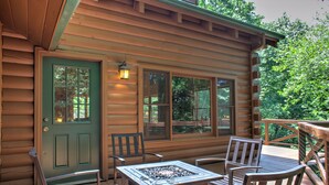 A wooden cabin with a deck, a door with a window, and a table with chairs. - Hot Tub, Pool Table & Fireplace + Biltmore Pass | Pet-Friendly Mountain Stay (Waynesville)