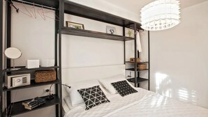 A modern bedroom with a bed, black shelving units, a hanging light fixture, and a small round mirror. -  Batchae, Two Bedroom Flat near Bačvice Beach (Split)