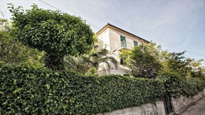 A building with a white facade, green shutters, and a stone wall with dense foliage. -  Batchae, Two Bedroom Flat near Bačvice Beach (Split)