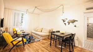 A modern living room with a sofa, yellow armchairs, a dining table with chairs, a world map on the wall, and a wooden floor. -  Batchae, Two Bedroom Flat near Bačvice Beach (Split)