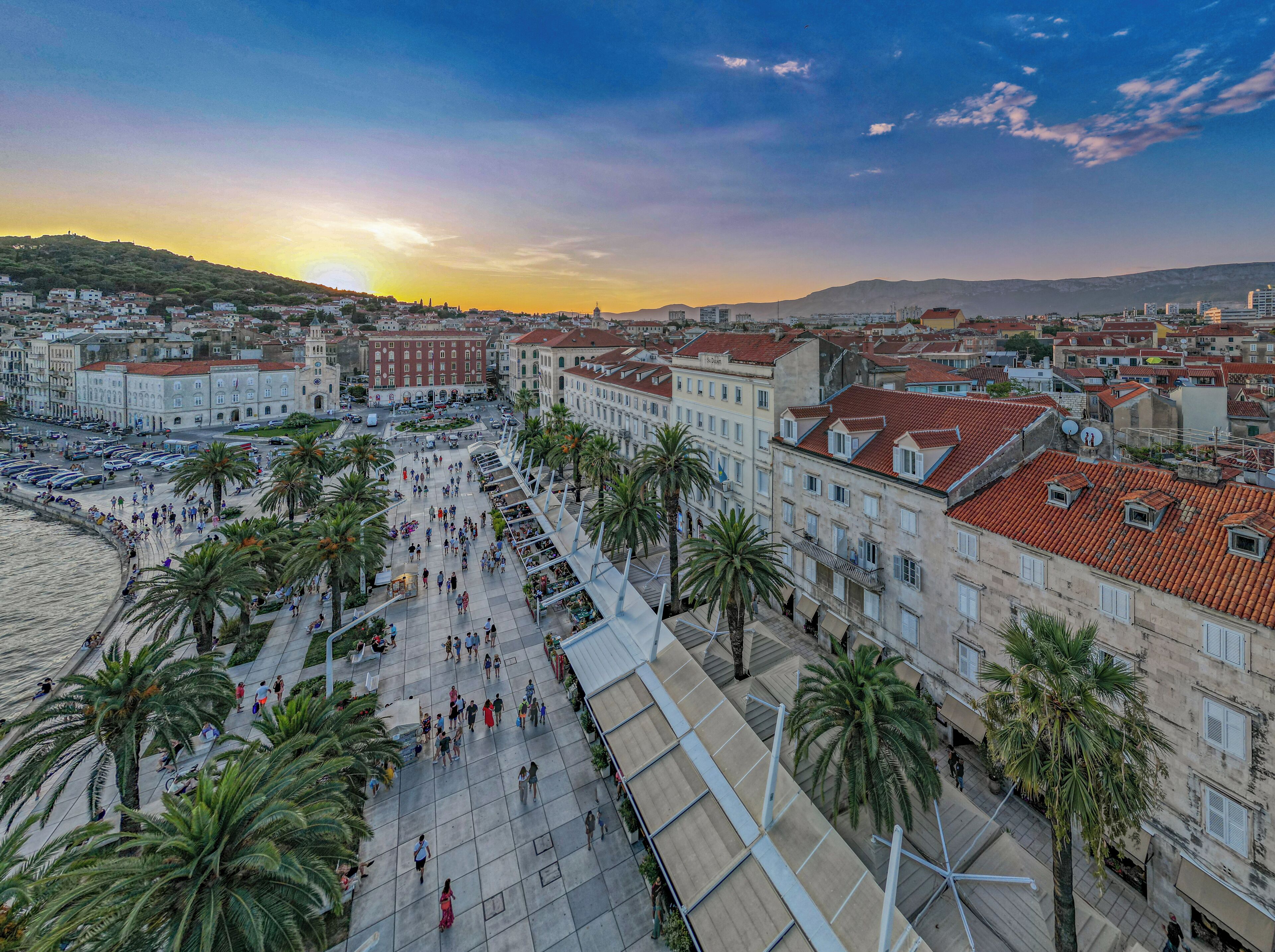 A coastal cityscape with a wide promenade lined with palm trees and historic buildings.