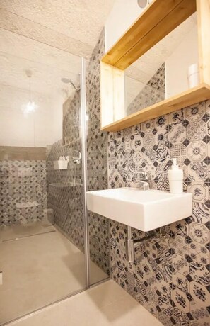 A bathroom with a glass shower enclosure, a white sink, and a mirror above it. The walls are tiled with a patterned design. -  Batchae, Two Bedroom Flat near Bačvice Beach (Split)