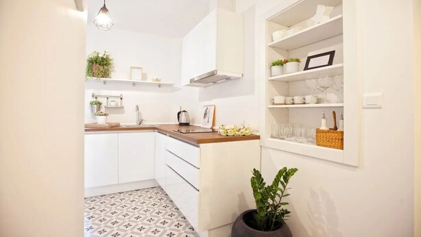 A modern kitchen with white cabinets, a wooden countertop, and a built-in shelf with glassware and plants. -  Batchae, Two Bedroom Flat near Bačvice Beach (Split)