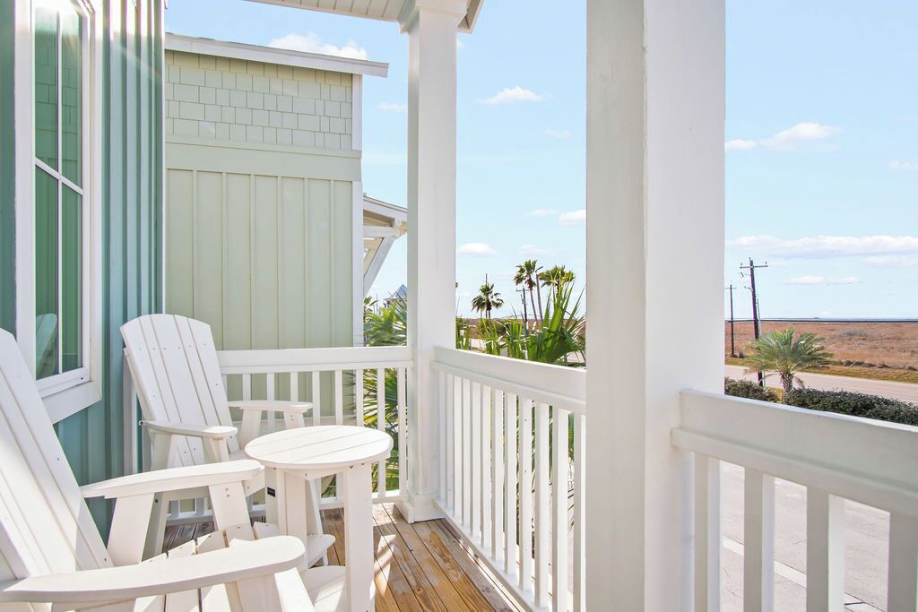 A porch with white chairs and a table, overlooking a desert landscape with palm trees.