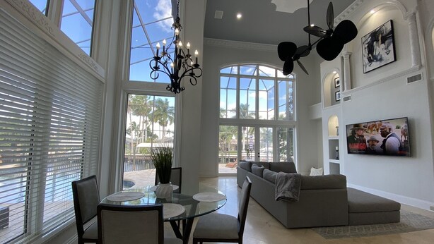 A spacious living room with a large window, a chandelier, and a ceiling fan. - Florida Modern Mediterranean Villa (Cape Coral)