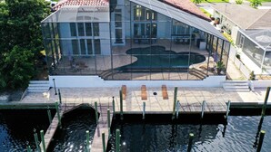 A modern house with a swimming pool, large windows, and a dock extending into a body of water. - Florida Modern Mediterranean Villa (Cape Coral)