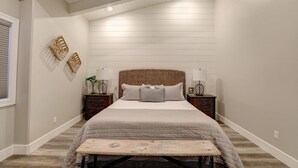 Een slaapkamer met een groot bed, twee nachtkastjes, een bankje en decoratieve wanddecoratie.
