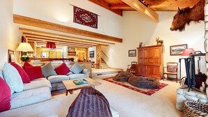 Amplia sala de estar con sofá, mesa de centro y chimenea. Se observa una escalera que conduce a un nivel superior.