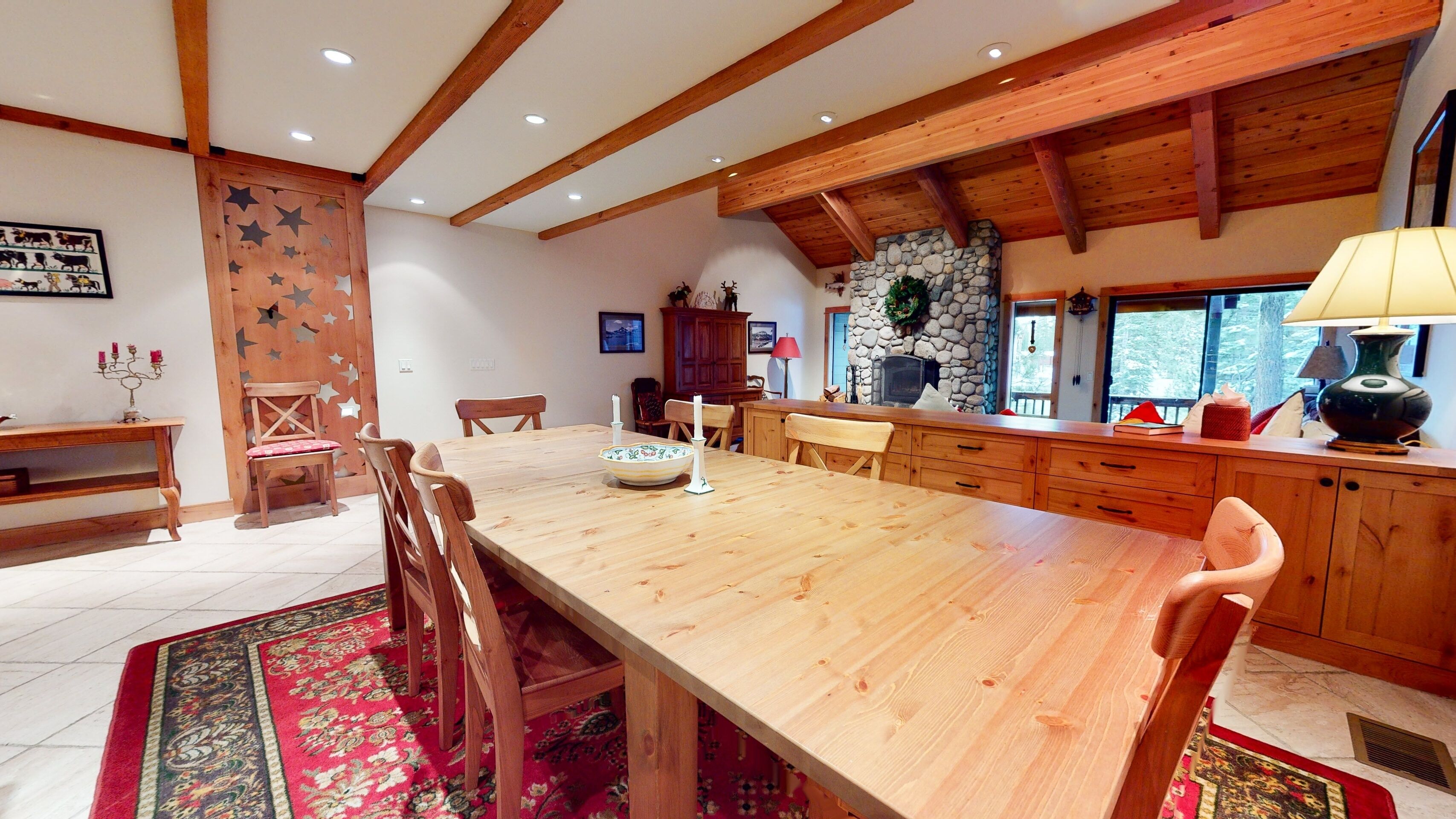 A spacious dining area with a long wooden table, wooden chairs, and a stone fireplace.