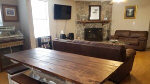 A wooden dining table with benches, a stone fireplace, a brown leather couch, and a television mounted on the wall. - Big Canal-front house, kayaks, canoes, game room, fish right from the dock. (Crawfordville)