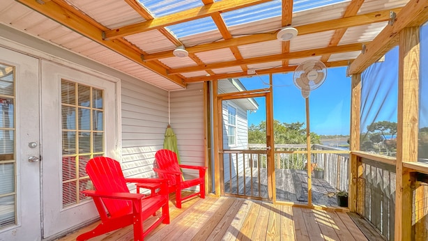 A covered porch with wooden flooring, two red Adirondack chairs, a green umbrella, and a view of a residential area. - Big Canal-front house, kayaks, canoes, game room, fish right from the dock. (Crawfordville)