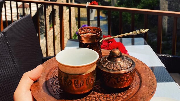 A table with a tray holding two copper cups and a sugar bowl, set against a scenic view of a village with a bridge and mountains.