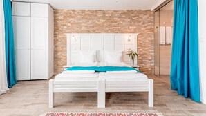 A bedroom with a white bed, a brick wall, and a chandelier.