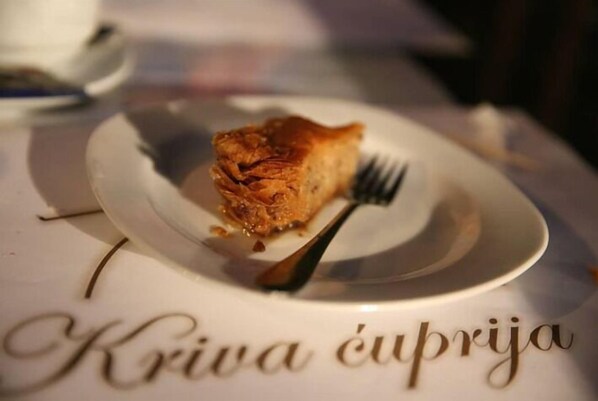 A plate with a piece of food and a fork on a table with a nameplate reading "Kriva Äuprija". - Hotel-Restaurant Kriva Cuprija (Mostar)