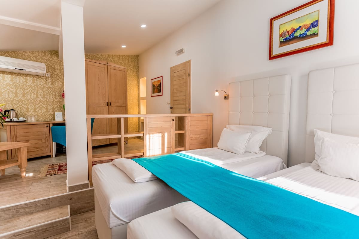 Une chambre d’hôtel avec deux lits, un bureau en bois, une kitchenette et une grande fenêtre.