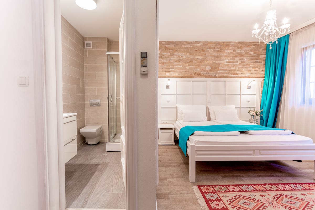 Une chambre moderne avec un lit blanc, un tapis à motifs rouges et blancs, un mur en briques apparentes et un espace douche.