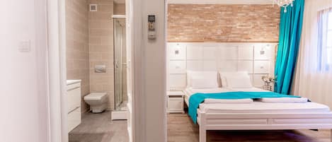 Ein modernes Schlafzimmer mit einem weißen Bett, einem Teppich in Rot-Weiß-Rautenmuster, einer Ziegelwand als Blickfang und einer Duschkabine.