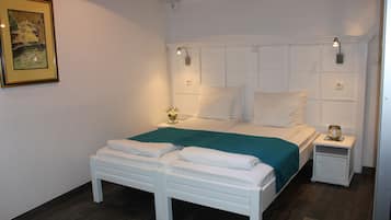 A neatly made bed with white linens and a teal throw, a small bedside table with a lamp, and a framed picture on the wall.