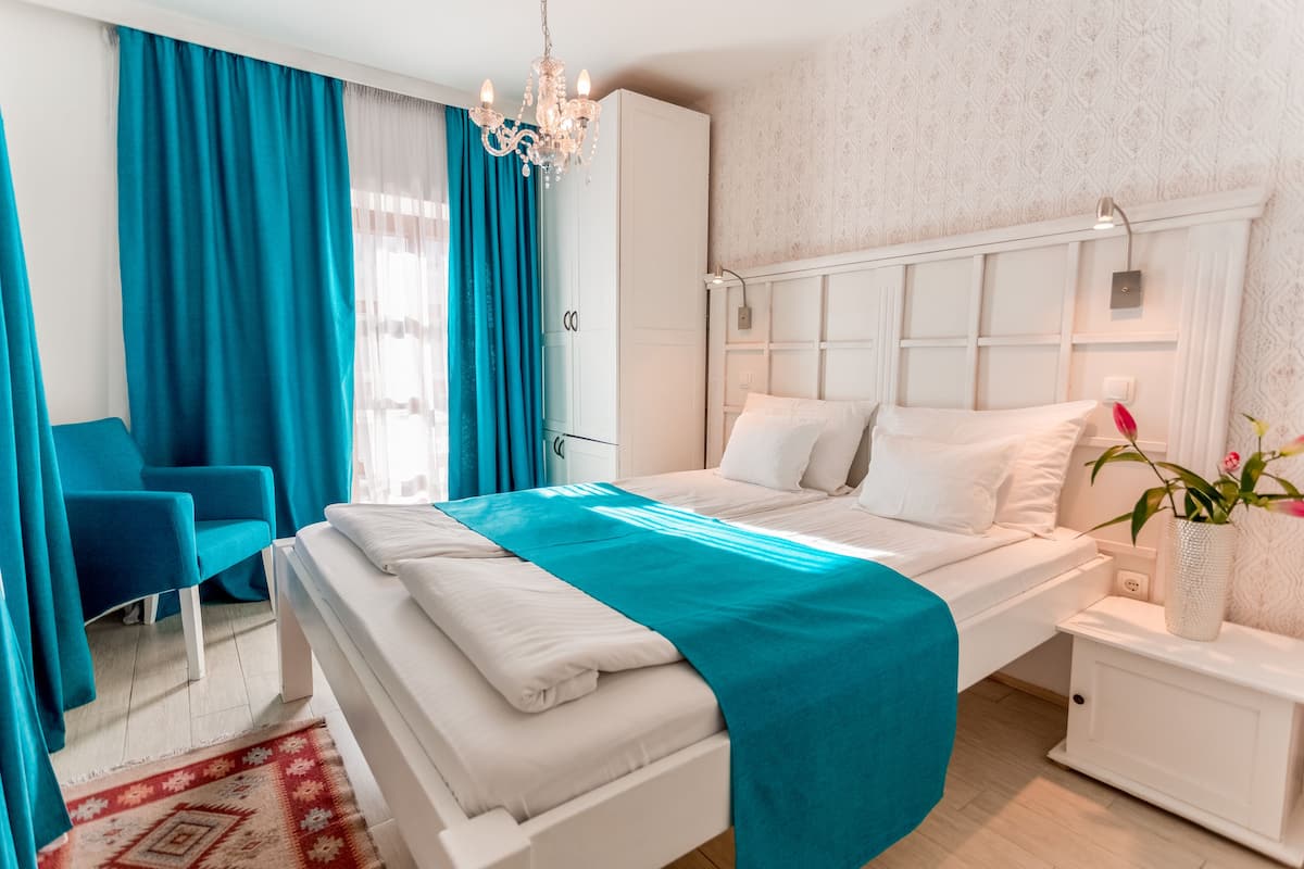 Une chambre à coucher moderne avec un lit, une table de chevet, une chaise, un lustre et une fenêtre avec des rideaux.