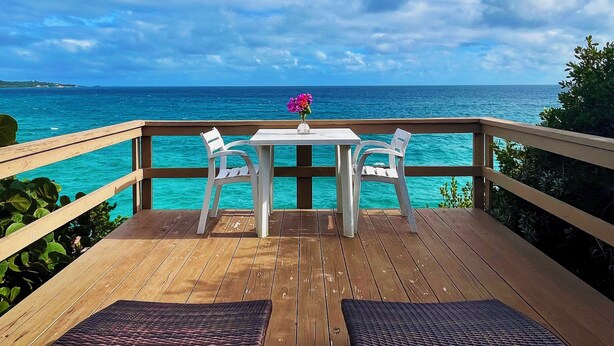 Un pontile di legno con due sedie bianche e un tavolo, con vista sul mare turchese sotto un cielo sereno.