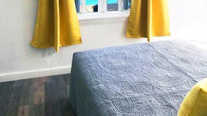 Una stanza con un letto, una finestra con tende gialle e vista sul mare.