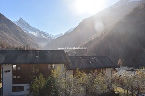Een gebouw in chaletstijl met een schuin dak, omgeven door een bergachtig landschap met besneeuwde toppen.
