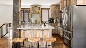 A kitchen with wooden cabinets, a stainless steel refrigerator, and a central island with stools. - NEW LISTING | 3BR Townhouse with AC, Pool, Golf, Tennis (Avon)