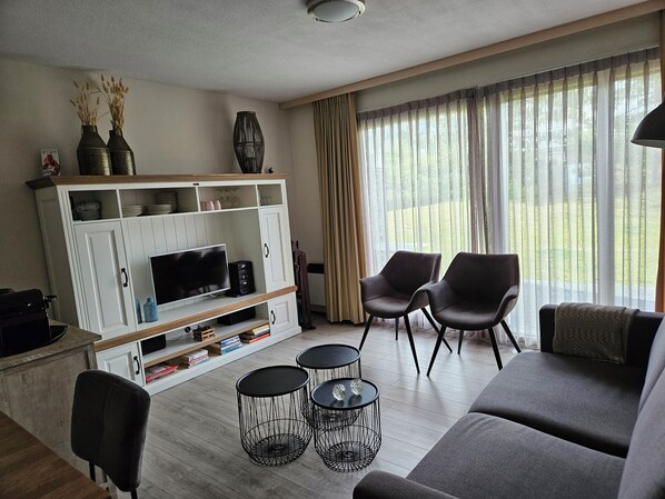 Ein modernes Wohnzimmer mit einer Couch, zwei Sesseln, einem Fernseher und einem Bücherregal.