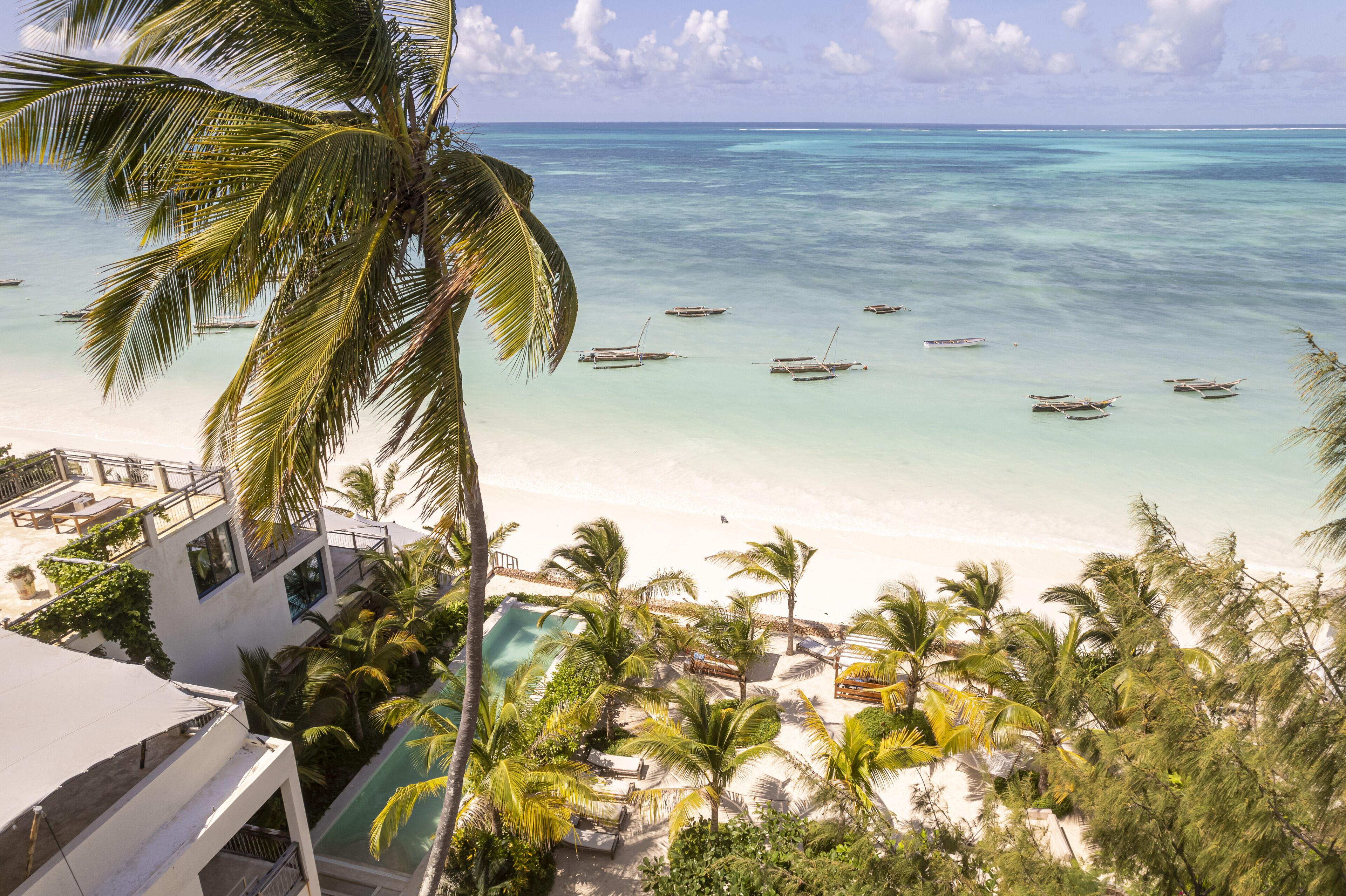 Vista de una playa con barcos, palmeras y una zona de piscina.