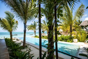 A pool area with palm trees, a thatched-roof building, and a view of the ocean. - Passion Boutique Hotel Zanzibar - Adults Only (Jambiani)