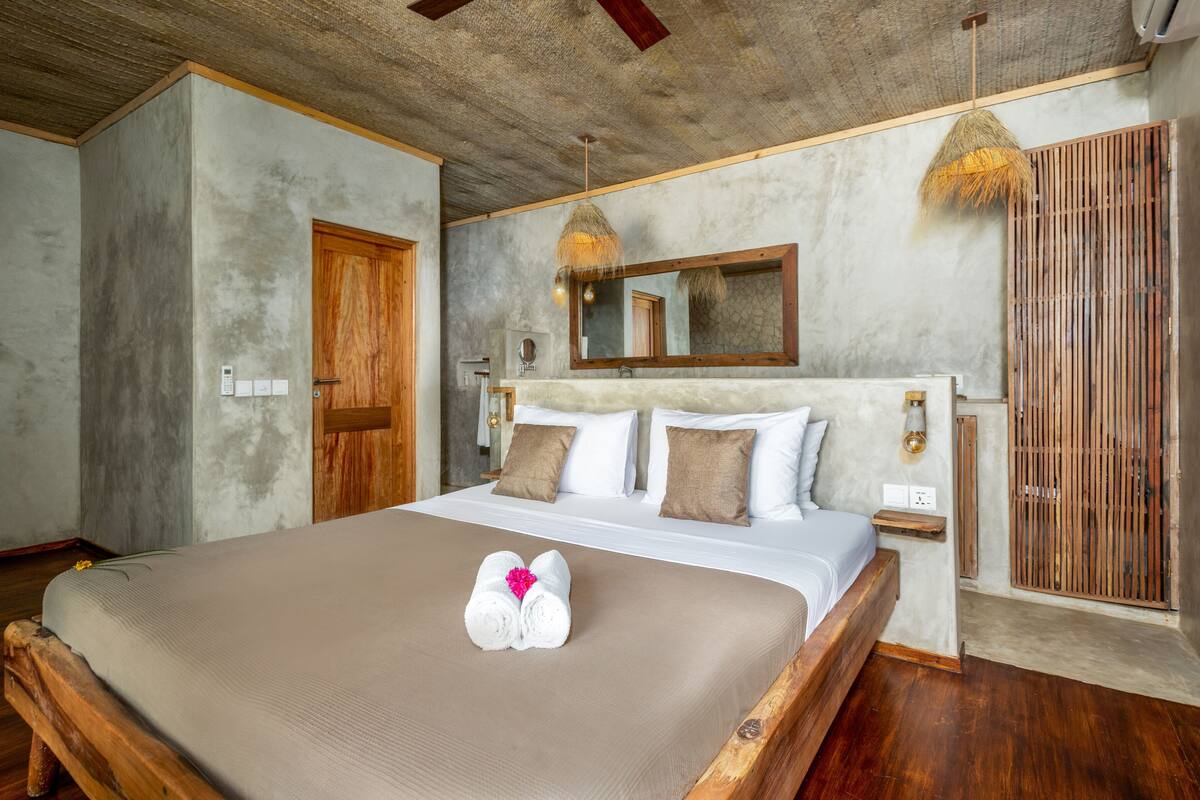 A bedroom with a large bed, wooden headboard, a wooden door, and a concrete ceiling.