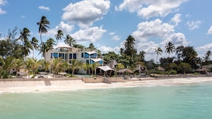 Una propiedad frente a la playa con un edificio de varios pisos, piscina y palmeras.