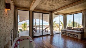 Ein geräumiges Zimmer mit einer großzügigen Badewanne, einem Sofa mit integriertem Bücherregal und einem Balkon mit Blick auf den Strand.