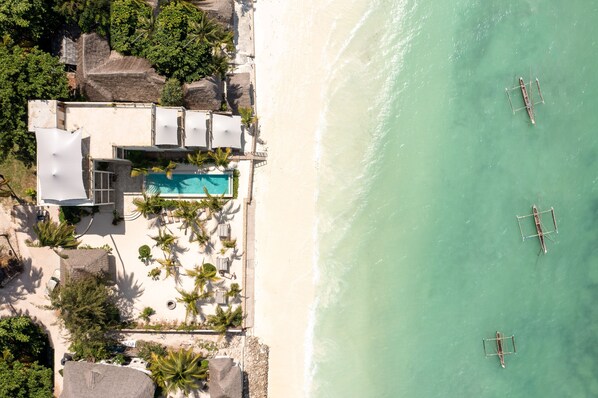An aerial view of a beachfront property with a swimming pool, palm trees, and a beach with three boats. - Passion Boutique Hotel Zanzibar - Adults Only (Jambiani)