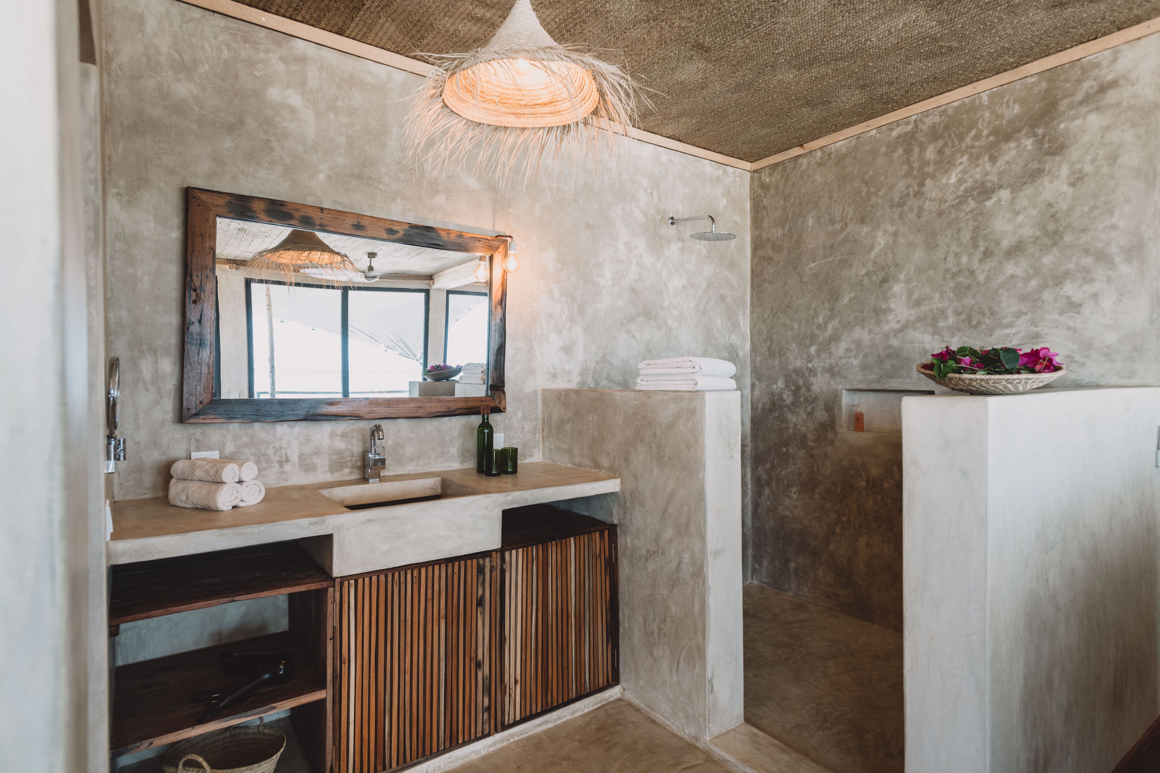 Un baño con pared de concreto, tocador de madera y lámpara colgante.