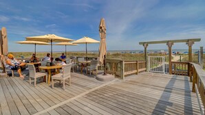A wooden deck with outdoor seating and umbrellas, overlooking a beach. - 2303 Seacrest - 2 Oceanfront Pools, Beach Bar, & Steps to the Beach! (Hilton Head Island)