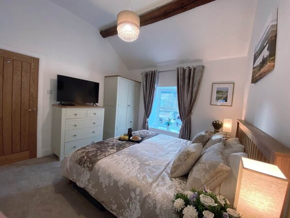 Une chambre à coucher comprenant un lit, une télévision, une armoire, une fenêtre avec des rideaux et un lustre.