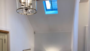 Een trap met een witte leuning, een klein dakvenster en wandlampen.
