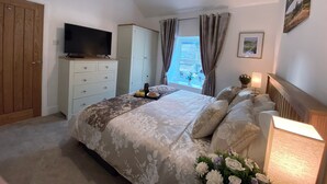 Een slaapkamer met een bed, een televisie, een dressoir, een raam met gordijnen en een schilderij aan de muur.