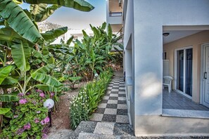 A checkered pathway leading to a building with a white exterior and a balcony with a white chair. - Bali Dorian Apartments (Mylopotamos)