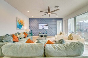 A modern living room with a sofa set, a flat-screen TV, and a ceiling fan.
