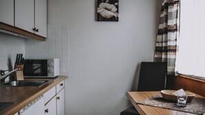 A kitchen with white cabinets, a microwave, and a sink. There is a dining table with a chair and a basket. - Landhaus Andrea (Saalbach-Hinterglemm)